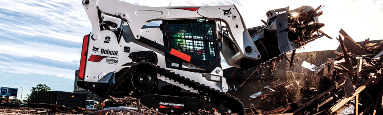 White Bobcat® excavator picking up piles of wood on a worksite on a cloudy day.